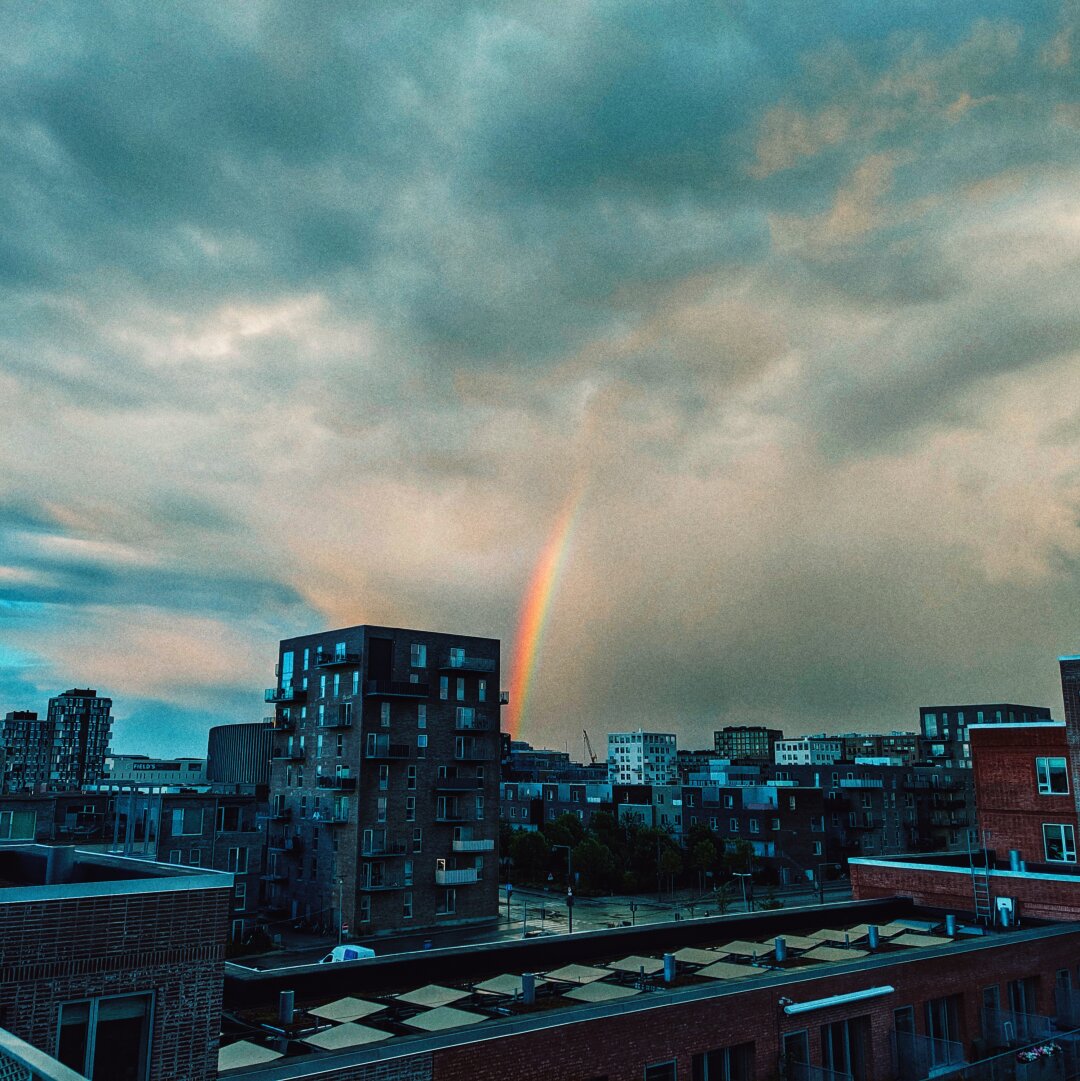 A rainbow behind buildings disappearing into the clouds