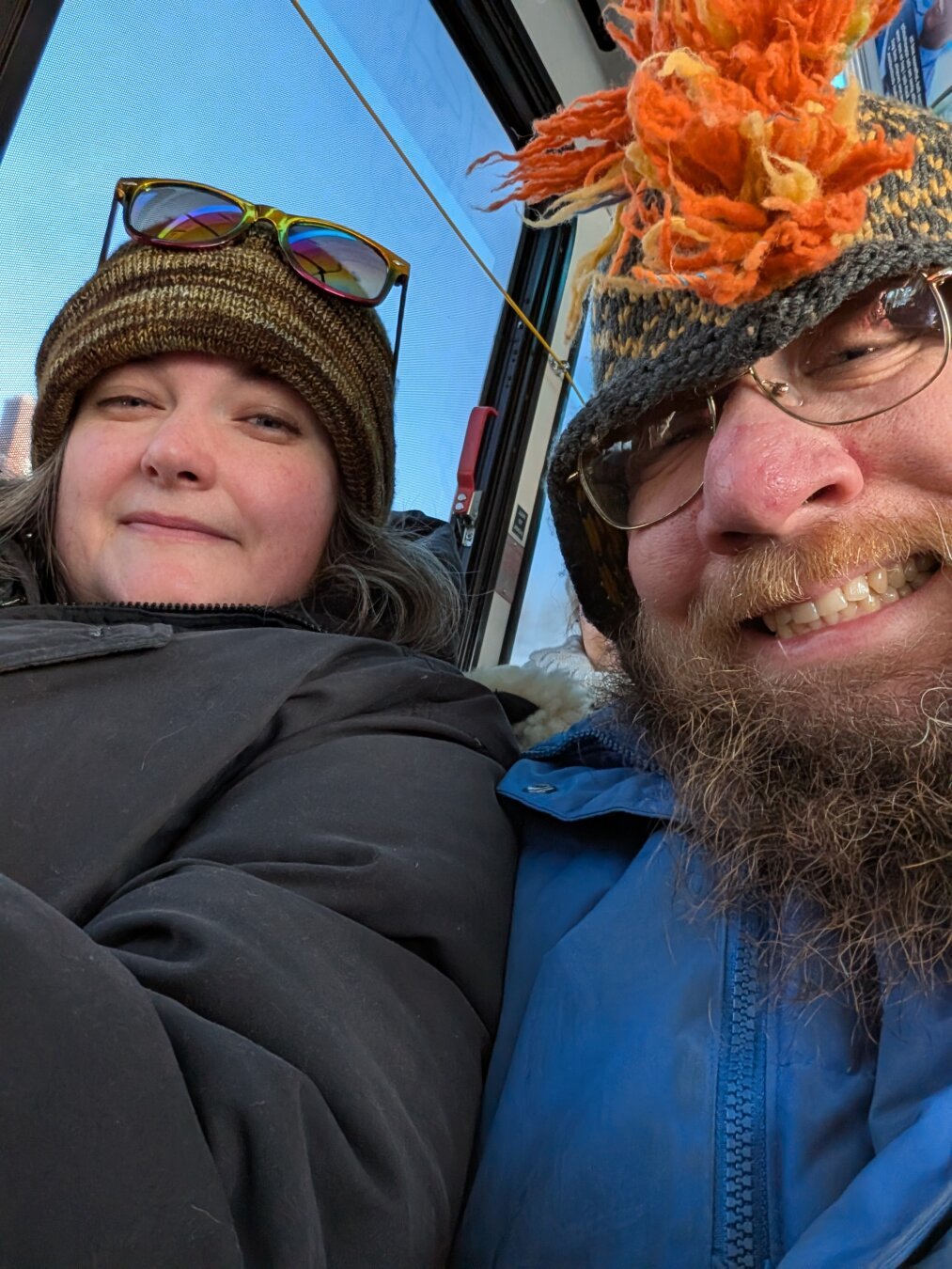 Two smiling people one a bus in winter coats and hats