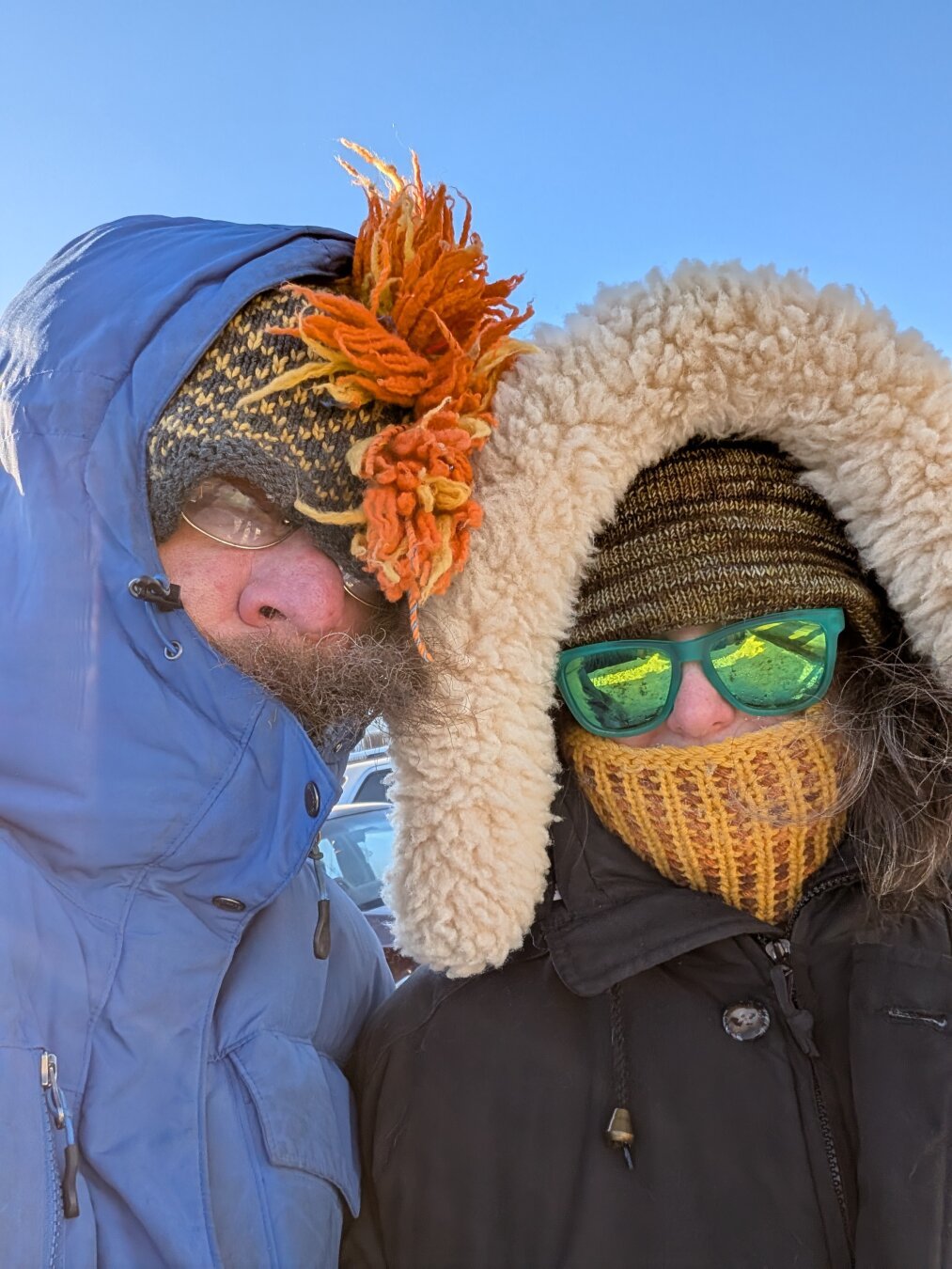 Two people huddled together in deep winter coats and hats with a blue sky in the background