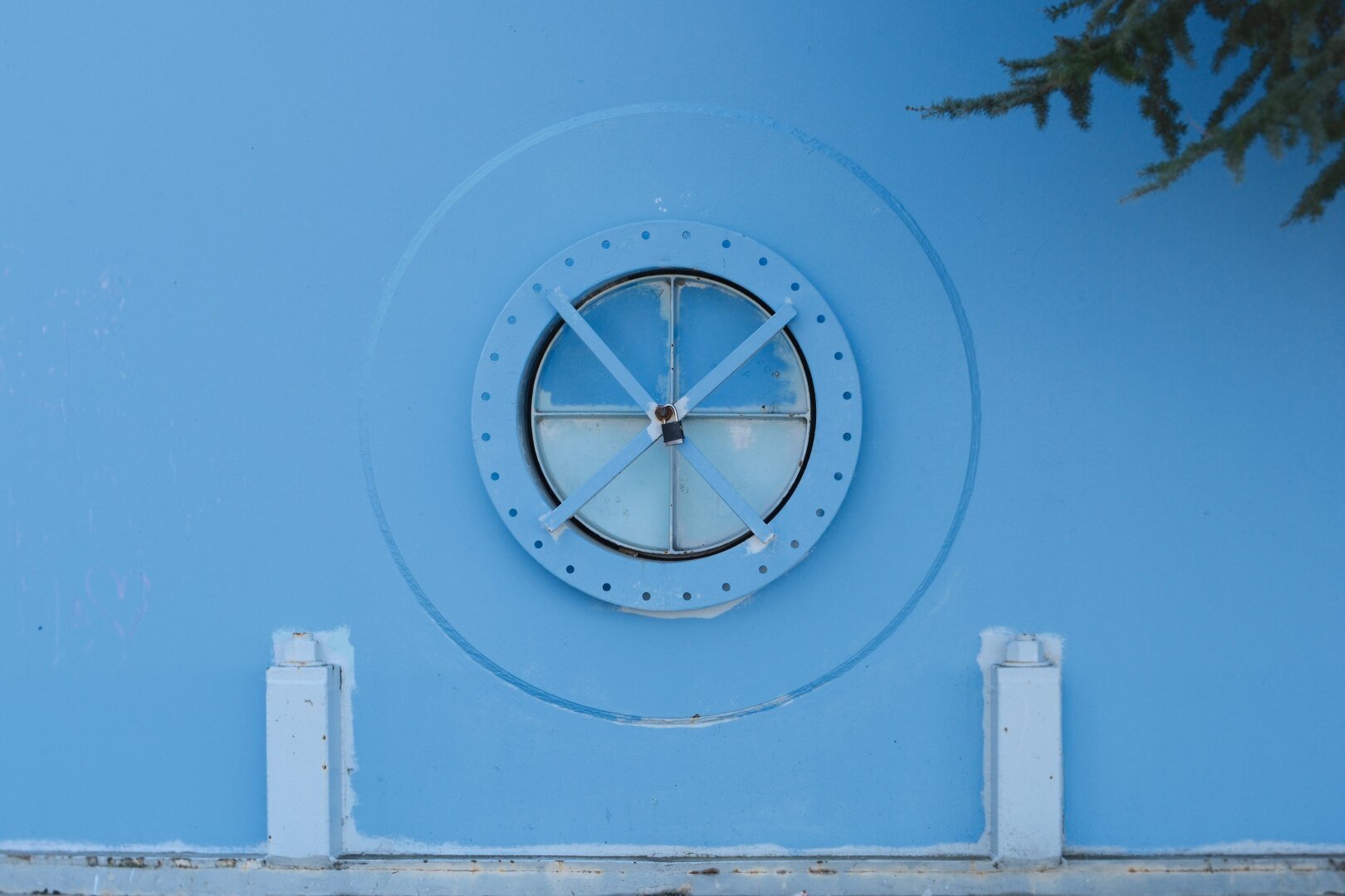 An access port on the side of a water tank. the tank and port are painted light blue. There is a tree branch entering from the top right corner of the photo.