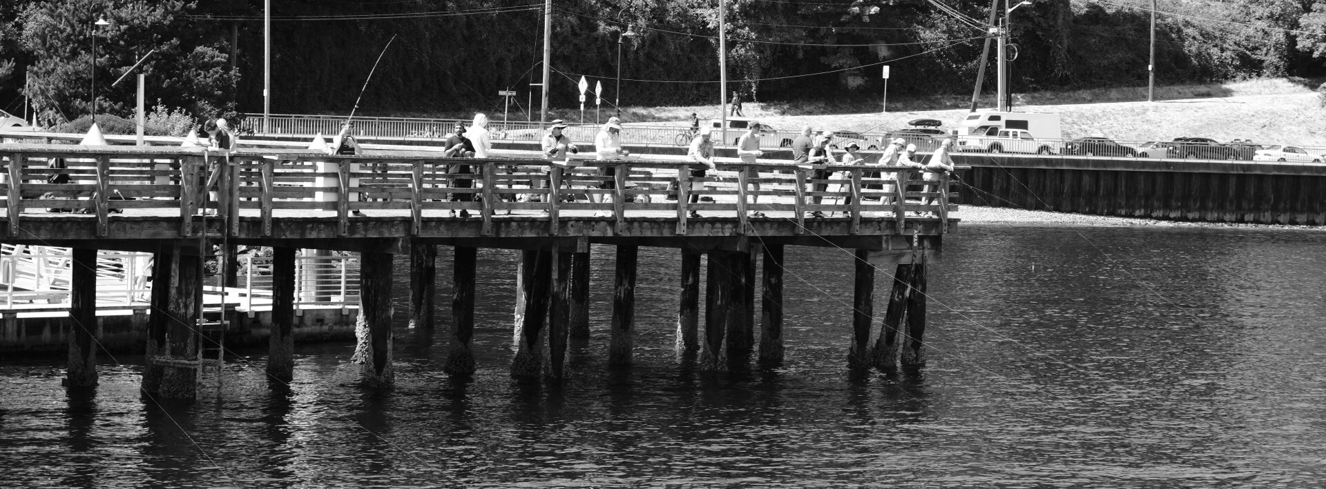 A black and white photo of people fishing off of a wharf.