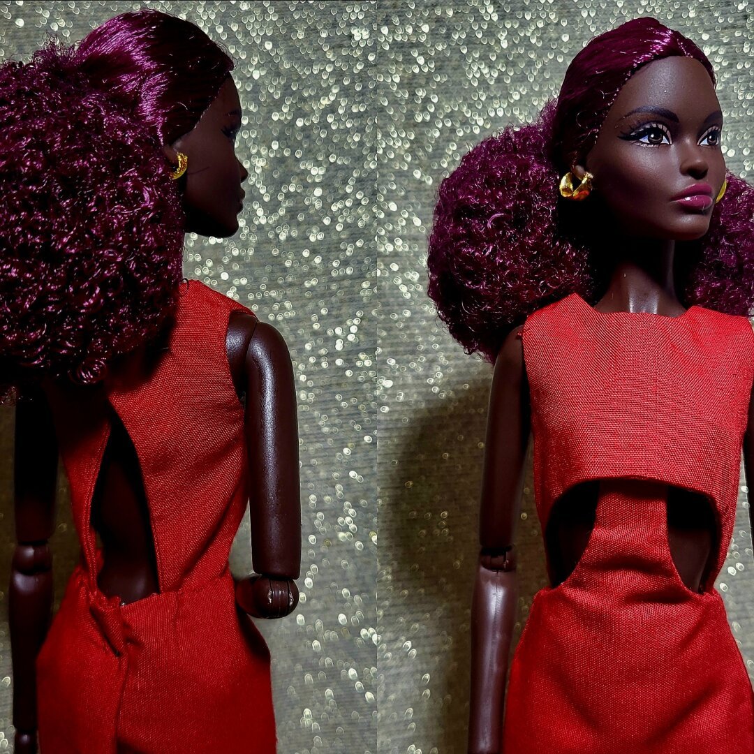 Black Barbie doll with curly burgundy hair wearing a read dress.