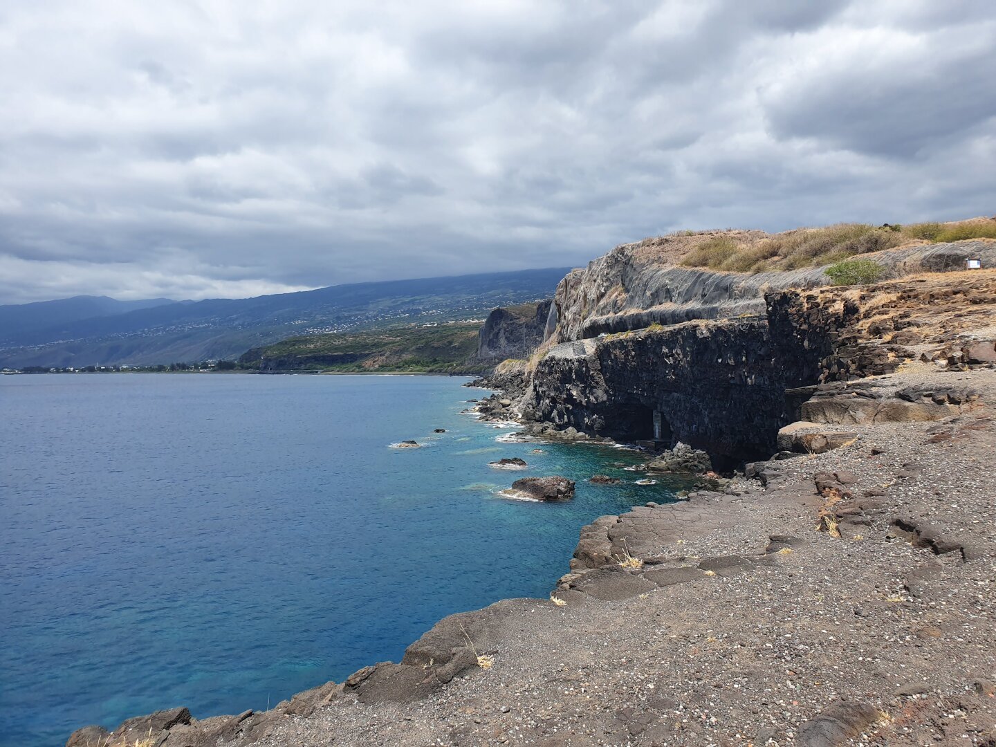 une petite falaise près de la mer, on peut voir une petite grotte sous la falaise, il y a des filets de protection sur les parois rocheuses qui longe la route au-dessus de la falaise