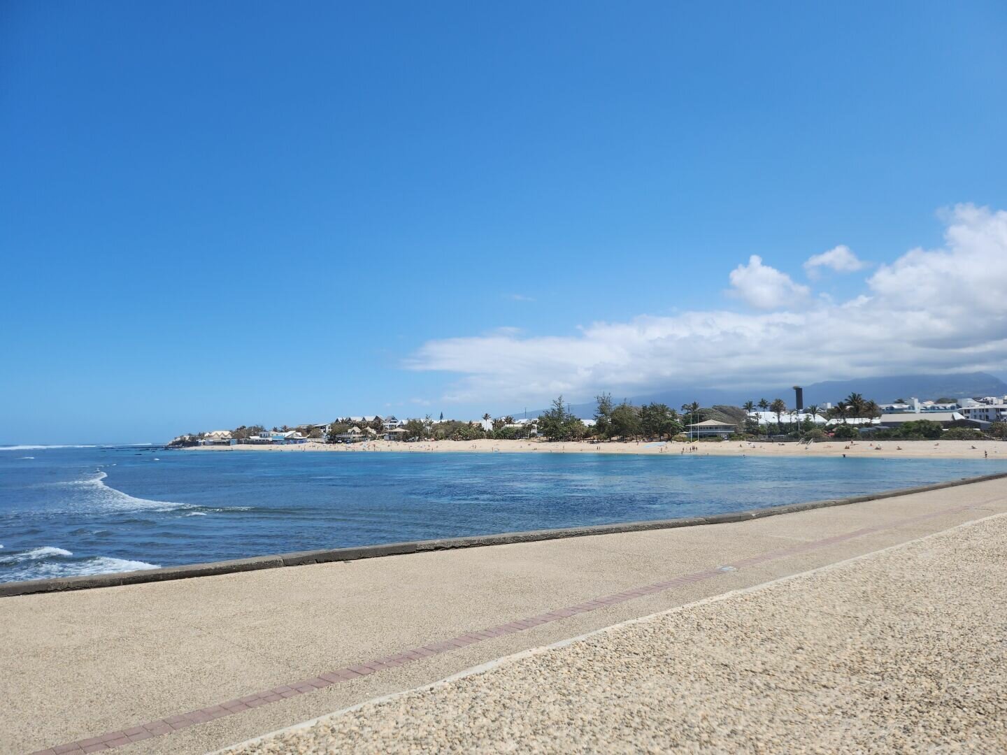 the sky is blue with a cloudy mass hiding the mountains, you can see the beach and the sea in the background