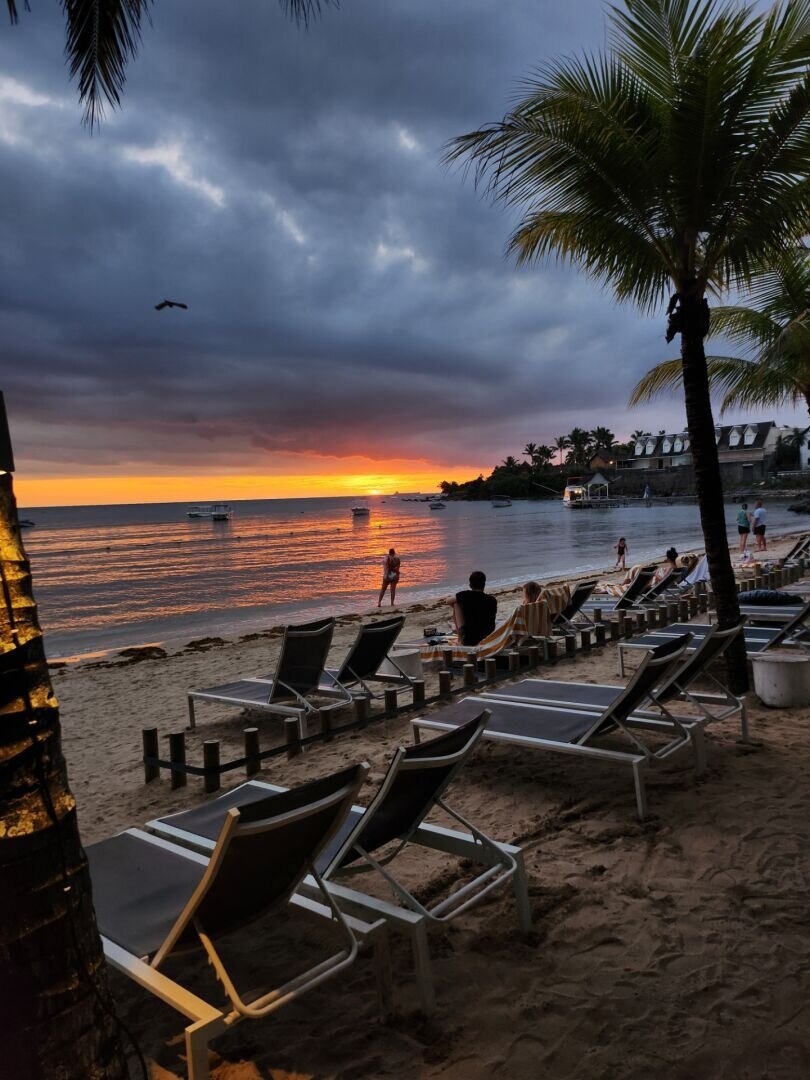 sunset under a cloudy mass on the beach, lots of deckchairs lined up on the sand, other people watching the sunset