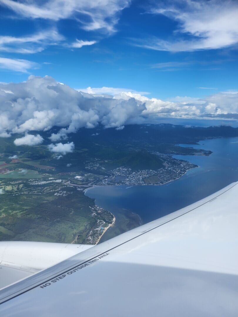 a view from an airplane window showing the right wing of the plane and the coast of Mauritius in cloudy weather.