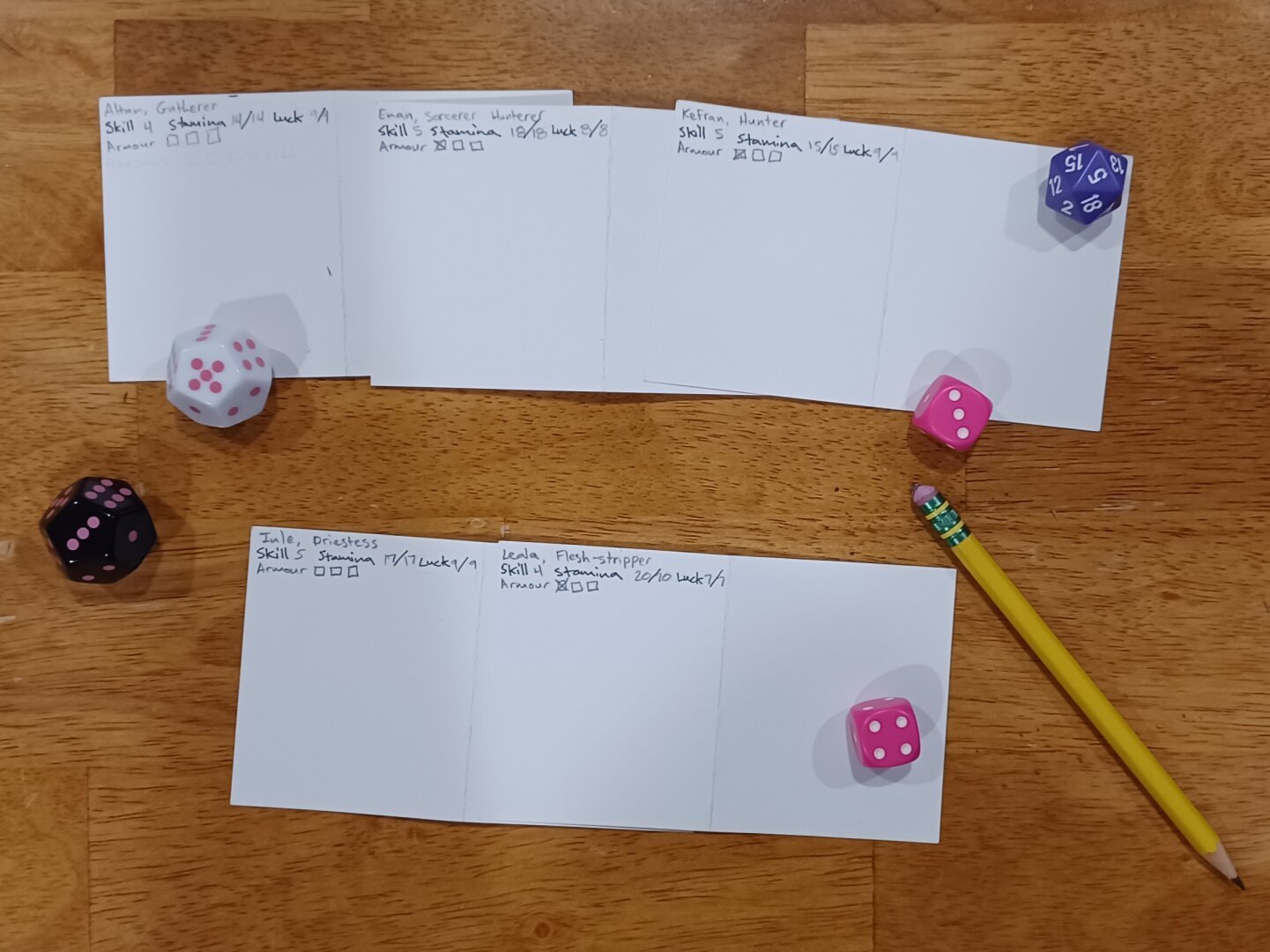 Five index cards arrayed alongside polyhedral dice and a pencil. The index cards are mostly blank, with just character name, background, skill, stamina, luck, and armour check boxes.