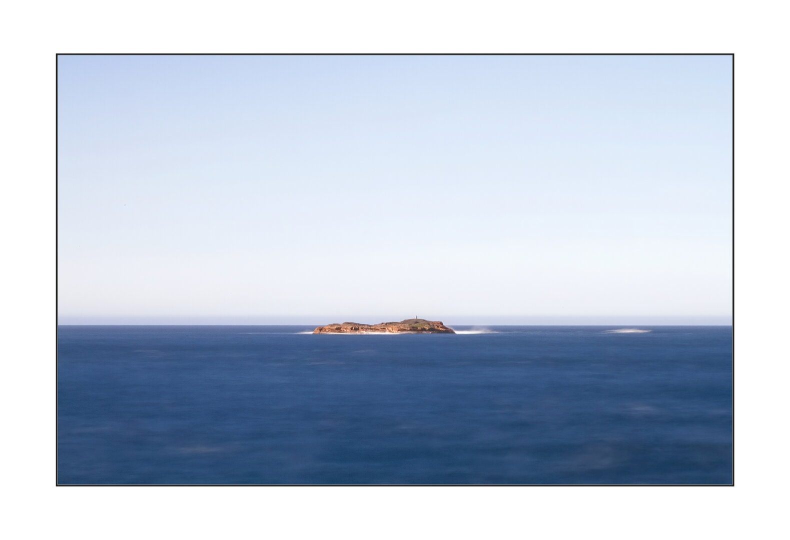 A distant small island on the blue ocean under the blue sky. Norway.