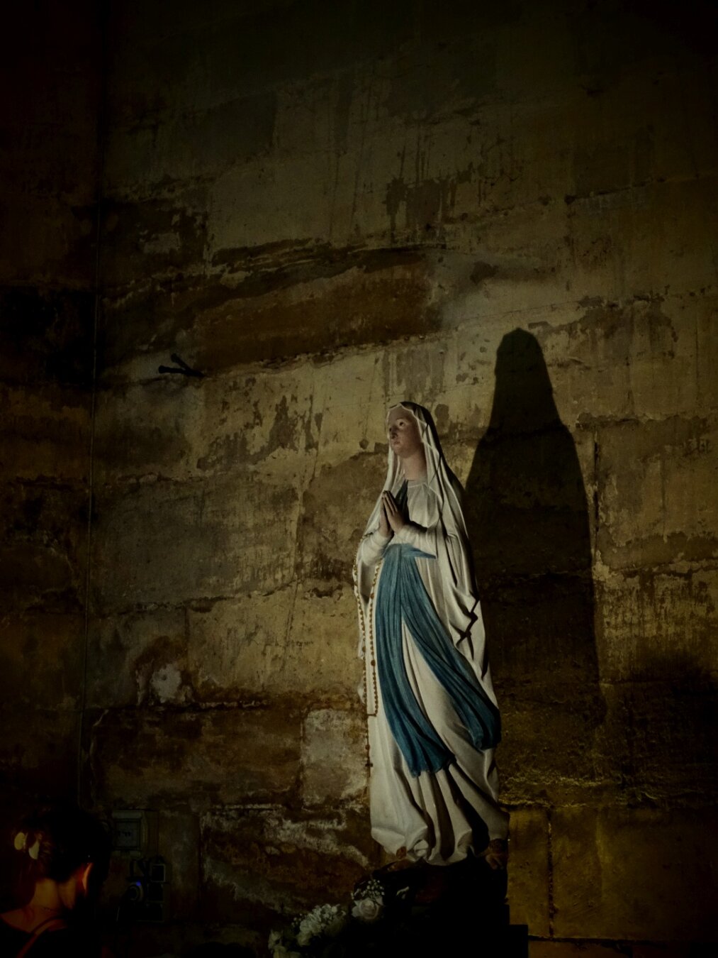 The Virgin Mary and her shadow in a cathedral. A worshipper prays.