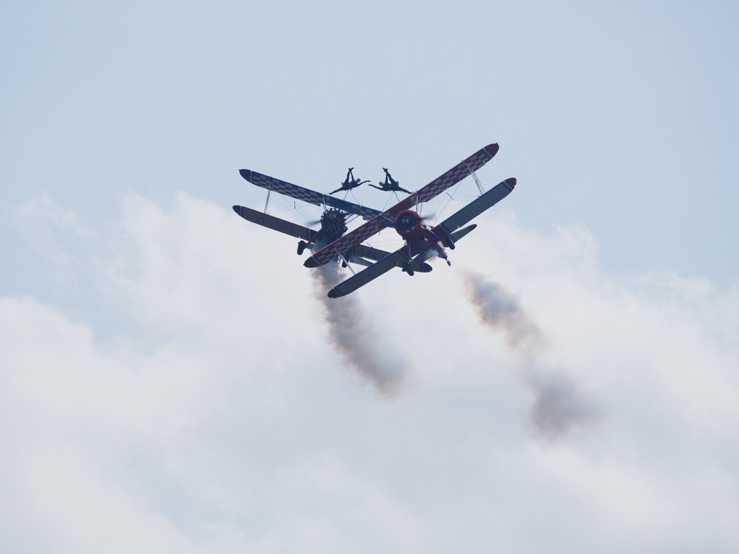 Two Boeing Stearman biplanes flying in formation. Each plane carries a harnessed wingwalker who performs synchronized acrobatics.