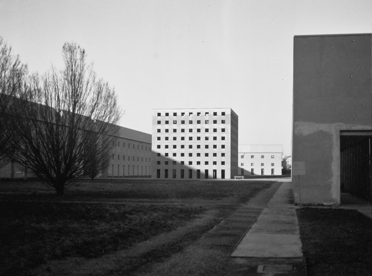 A black and white picture of an example of modern architecture: Aldo Rossi's cemetery is a simple cube of concrete with seven rows of square openings and nine rectangular portals opening at its base to grant access.