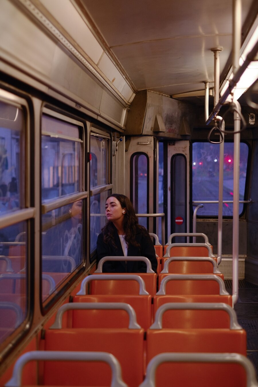 A girl craning her neck to look outside of the fogged window in a tram, Milan, Italy. The light is very cinematic, hues of purple and orange fighting for dominance in the scene