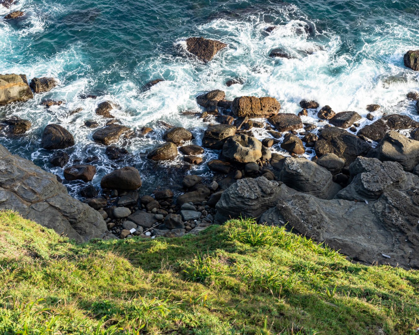 ocean above rocks above grass