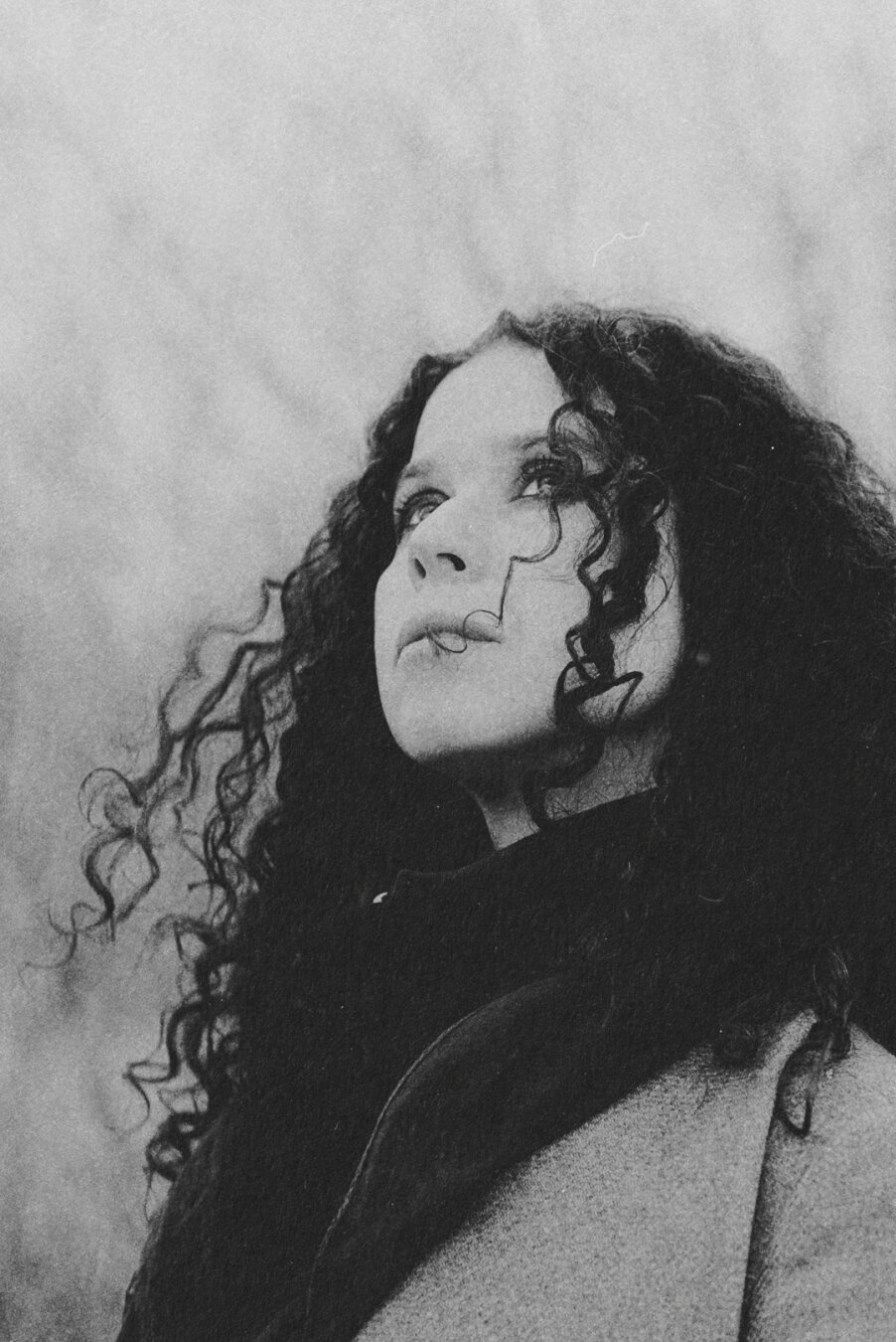 Black and white portrait of woman looking up, hair moved by wind.