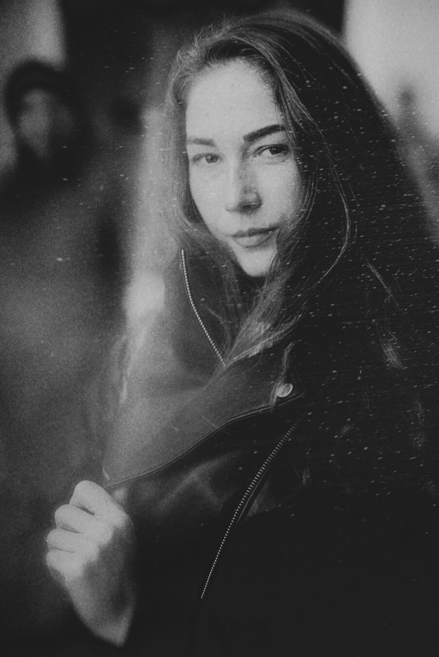 Grayscale photo of a woman with long fluffy hair hiding from cold in black jacket.