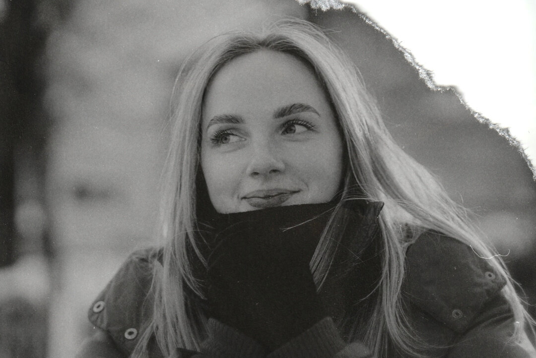 Grayscale photo of a light haired woman in winter clothes subtly smiling.