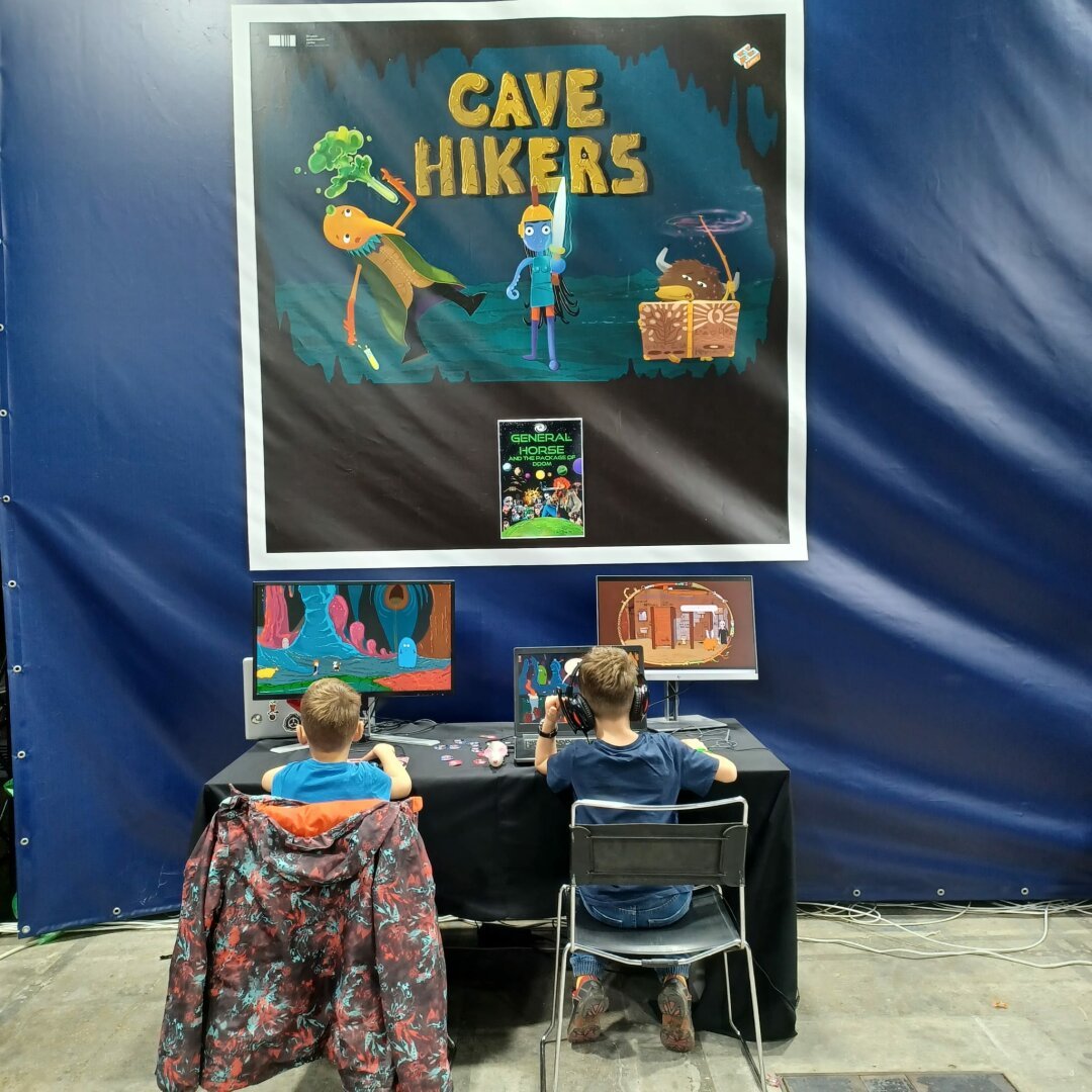 two kids from the back, each playing their own copy of Cave Hikers under a large poster of Cave Hikers