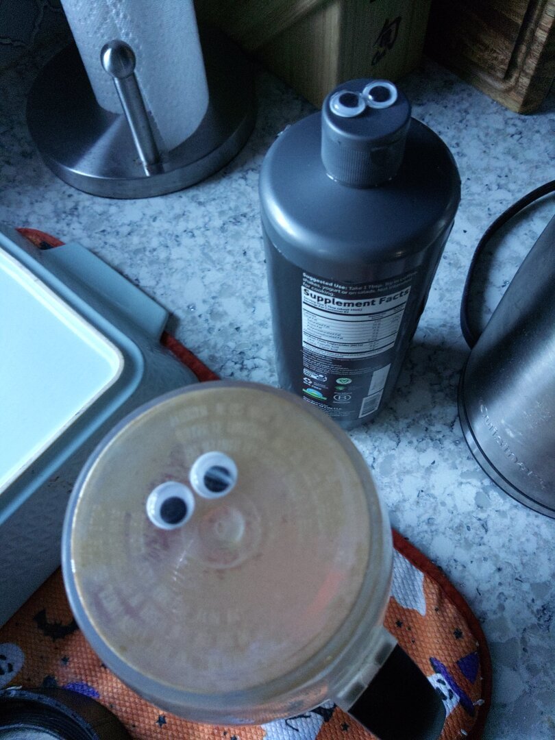 A cup of iced coffee and a bottle of MCT oil with googly eyes placed on them.