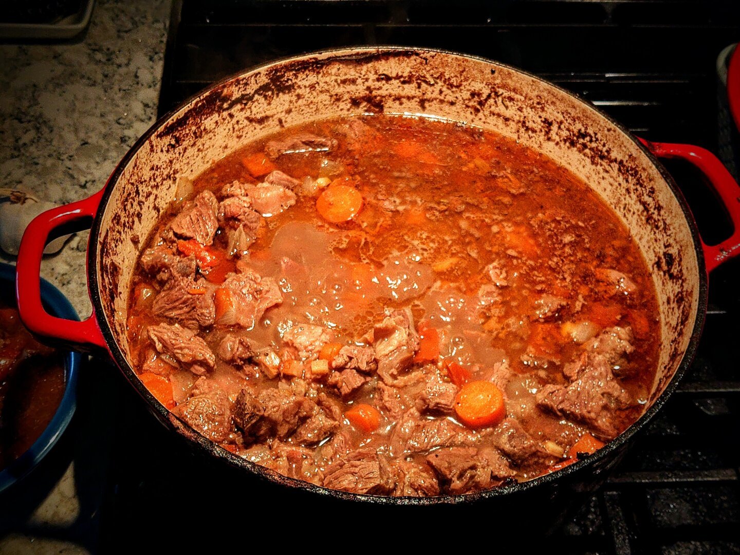 A large red cast iron pot of beef stew is simmering on the stove.