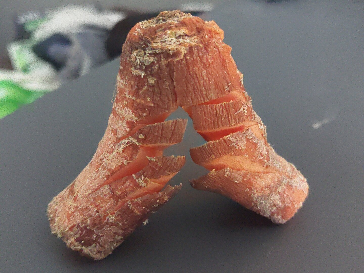 A piece of an old, crusty carrot, split in half with various cuts across it. It was photographed on my desk today. It has since been thrown in the trash.