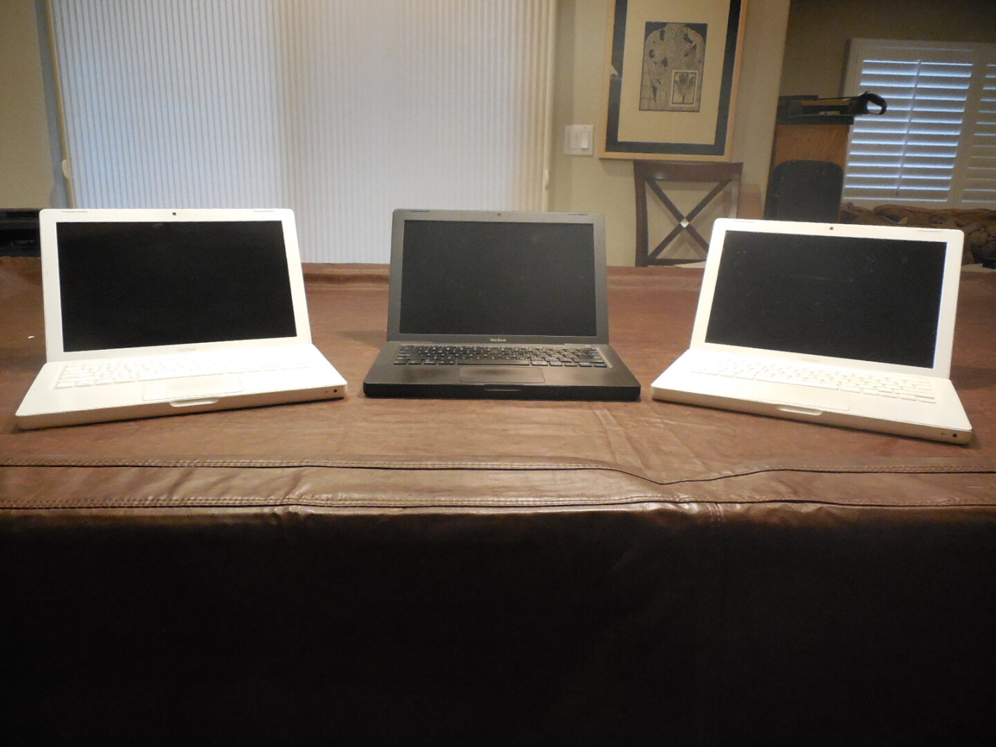 Three 2007 MacBooks sitting on a covered pool table. The two on the outside are white, and the one in the middle is black.
