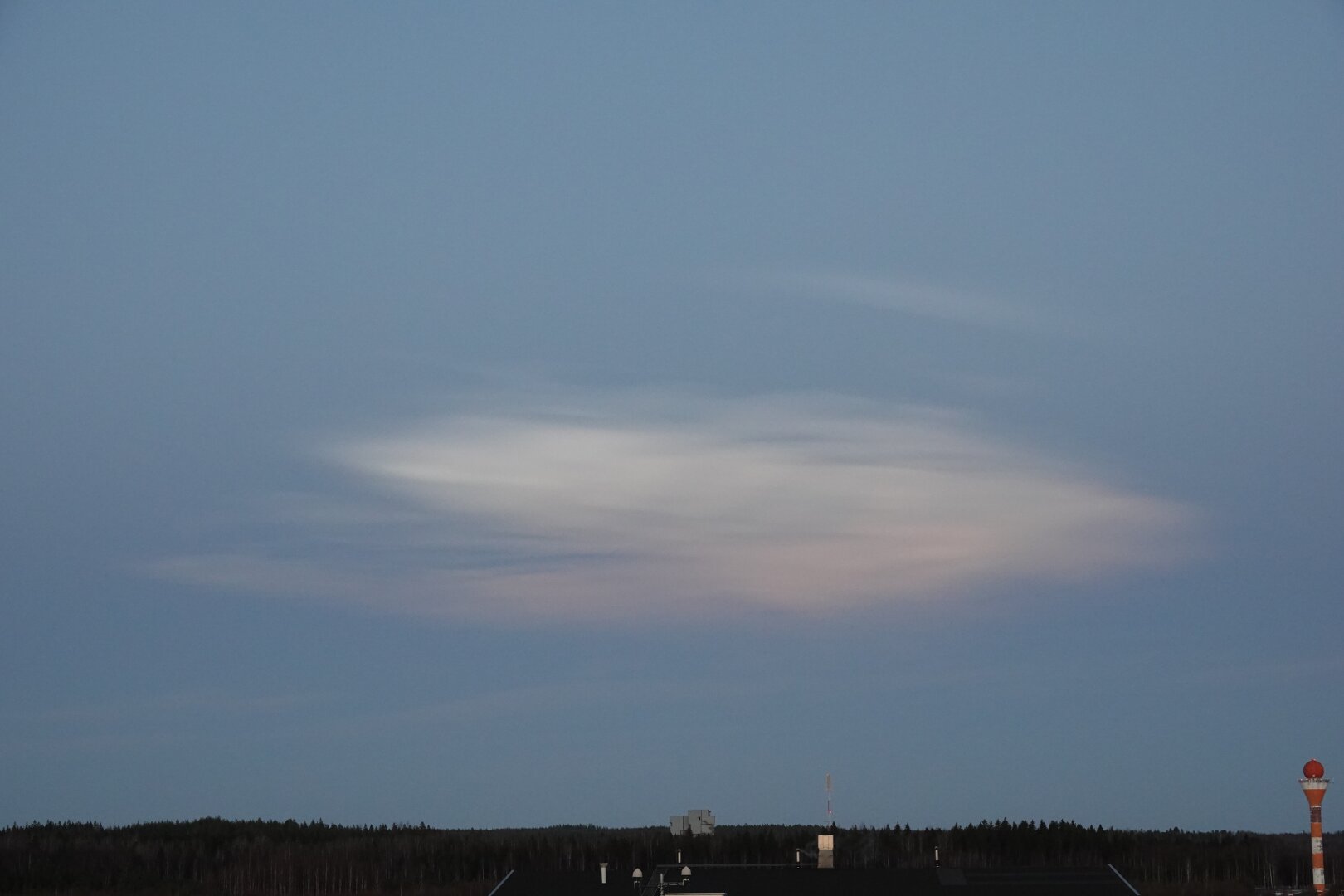 A pale white cloud on the darkening evening sky. The edges of the cloud are somewhat fuzzy. It has a slight orange tint at the bottom edge, as the sunset creeps up to its level.