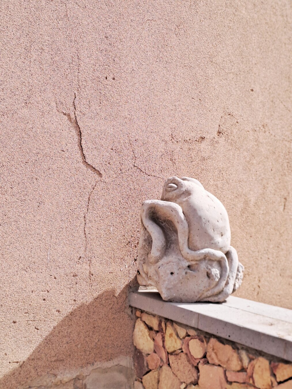 A small stone sculpture depicts an octopus. It is placed on the balustrade of a small wall that delimits the entrance to a house.