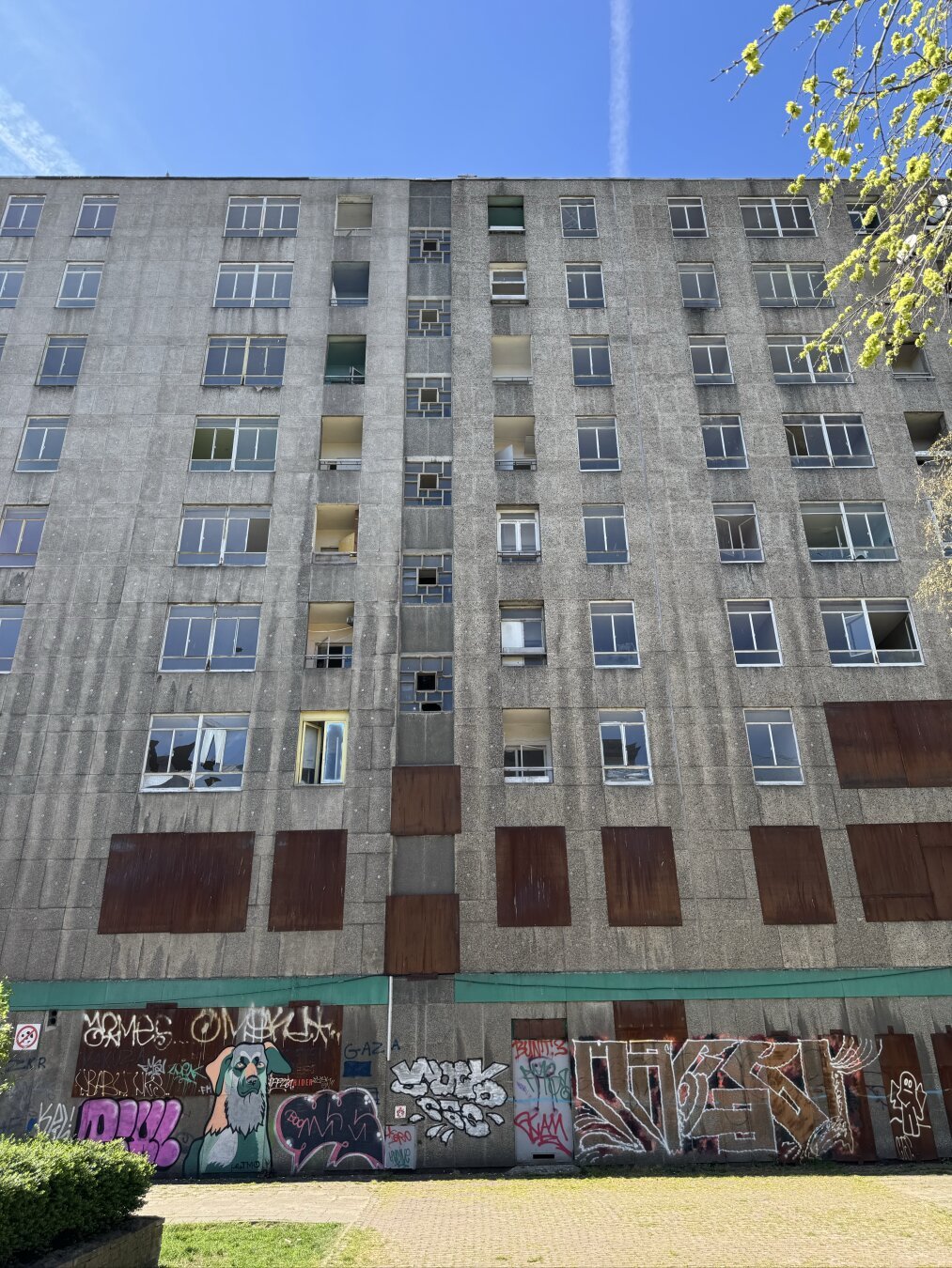 A concrete appartment building from 1963, run down, and with windows covered up with rusted iron plates.