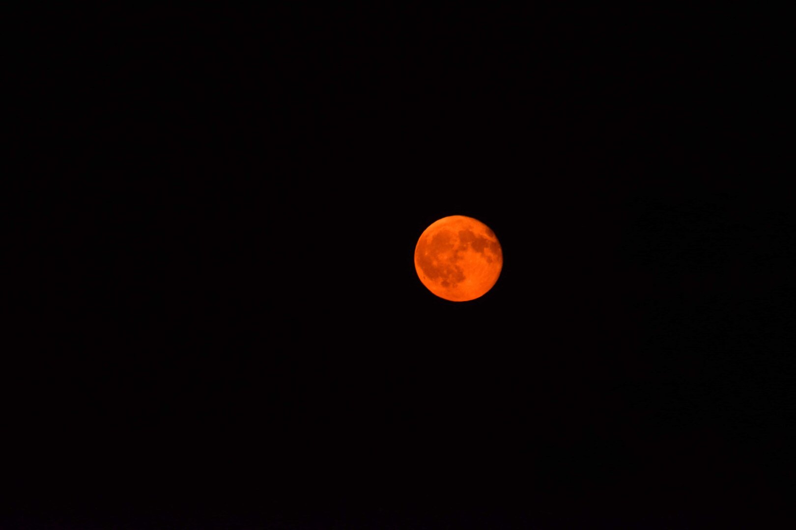 Orange full moon with visible surface shading, positioned slightly right of center against a black night sky.