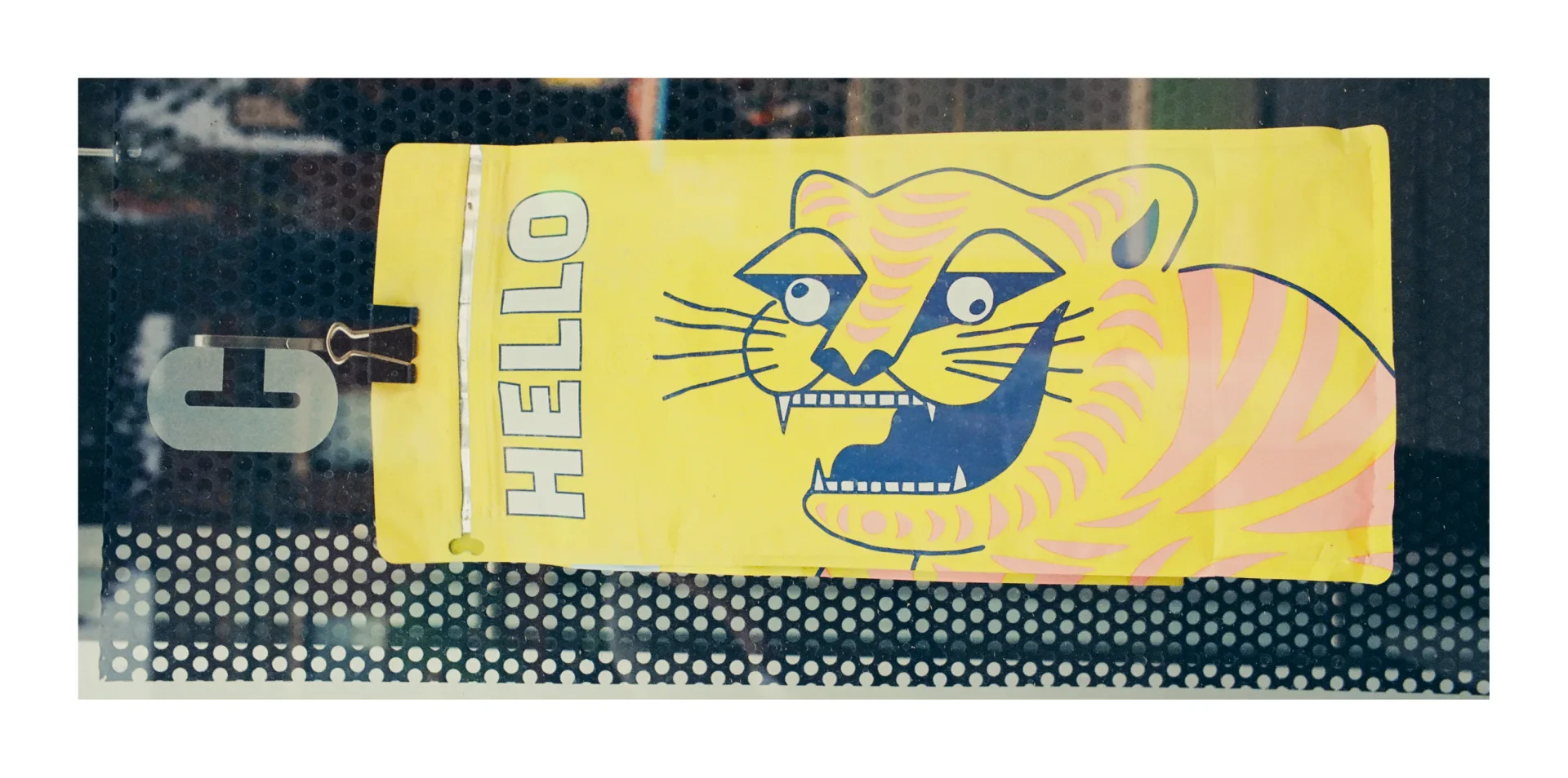 A colour photograph of a coffee bag displayed in a coffee shop window. The bag has a cartoon of a cross-eyed tiger with the text "HELLO" beside it.