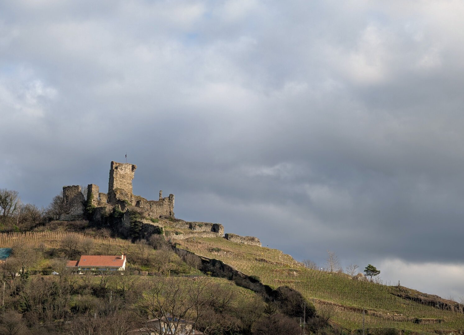 Old ruined castle on top of a hill. The sky is cloudy yet very bright, casting lights and shadows on the grass of the hill.