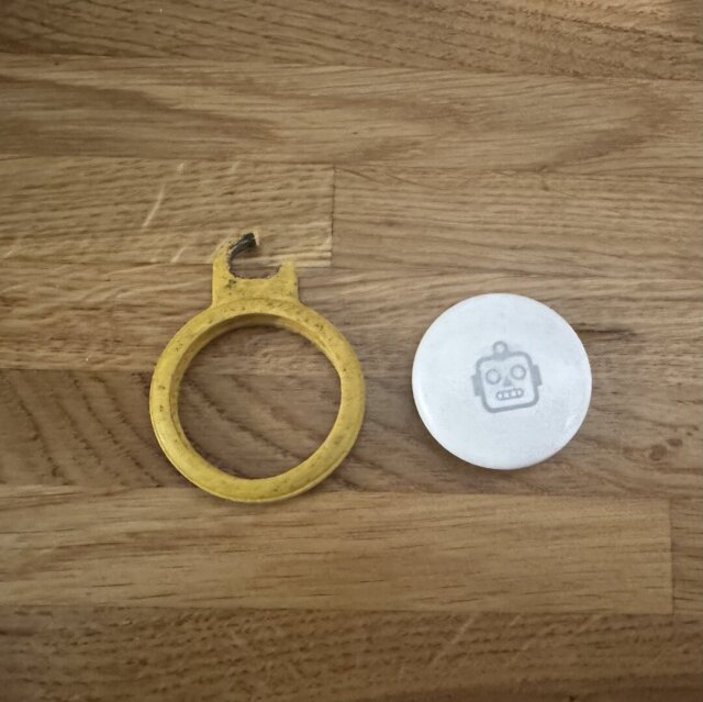 An AirTag with a robot on it next to a yellow keyring holder that’s broken