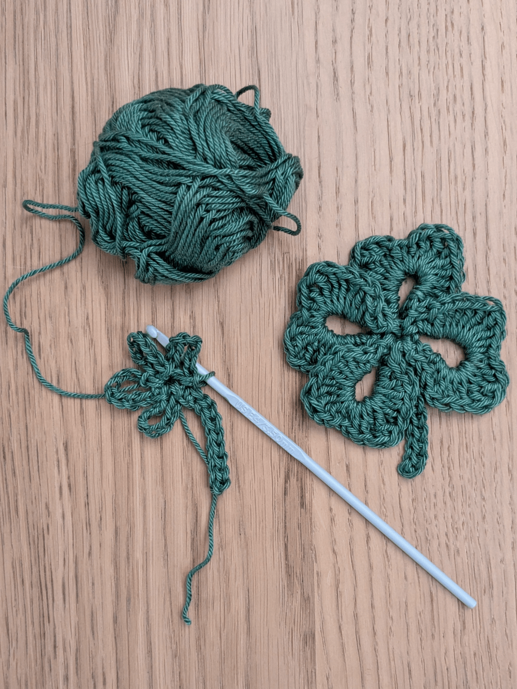 four leafed clover crocheted in green cotton yarn, and another partially formed leaf on the crochet hook