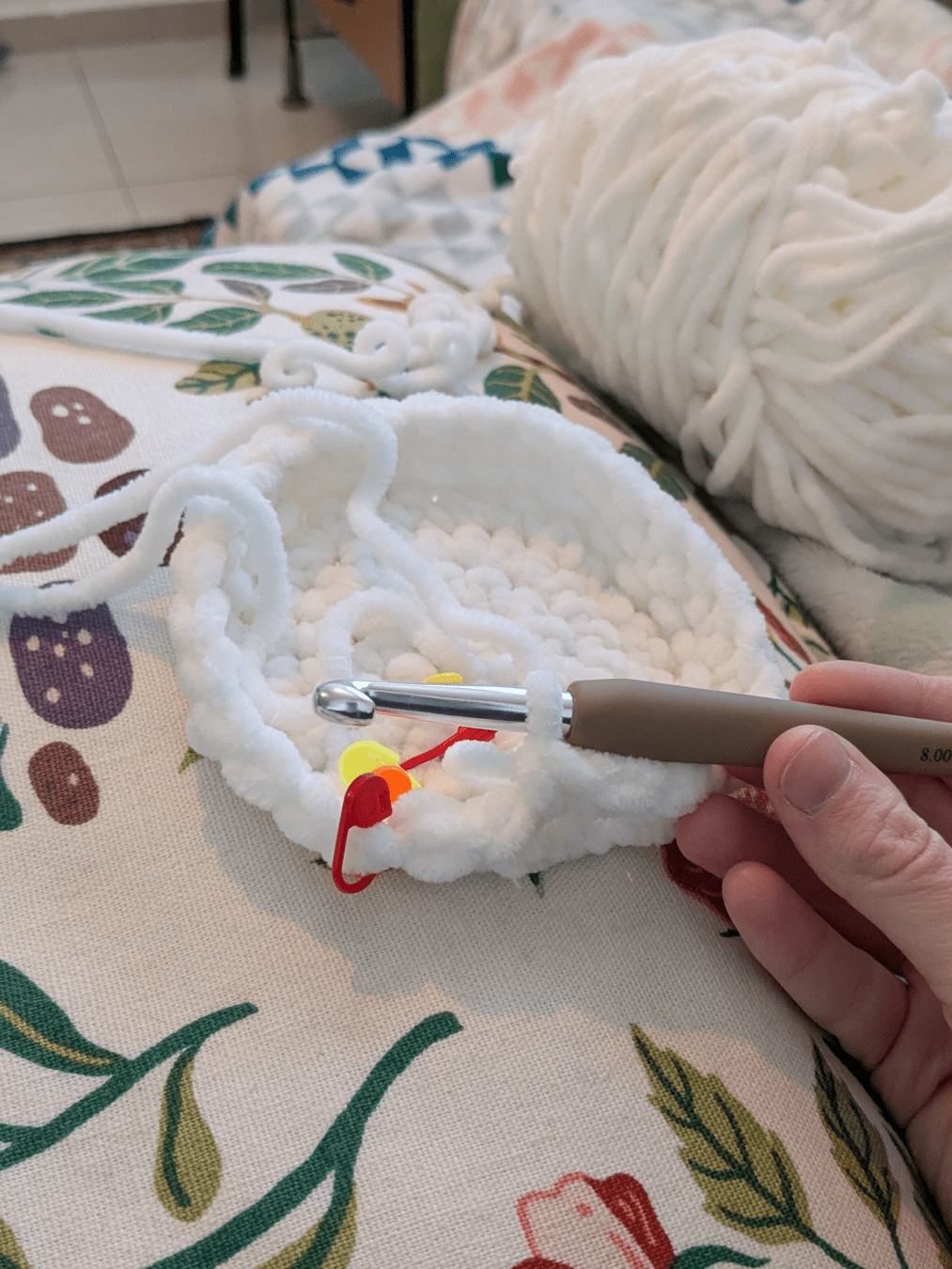 crochet worked in the round in white fluffy chenille yarn on a thick hook, the base is about the size of a hand and the rounds are starting to stack up to create sides