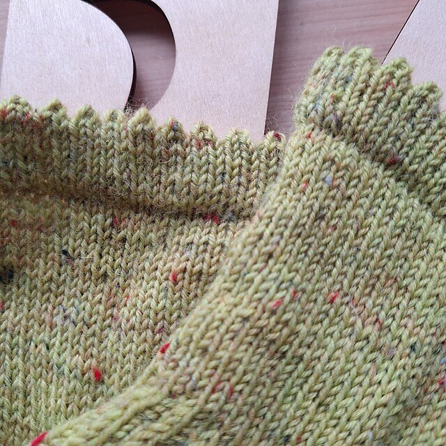 A close up of the picot border of handknit green socks, with a bit of wooden sock blockers and a wooden table in the background