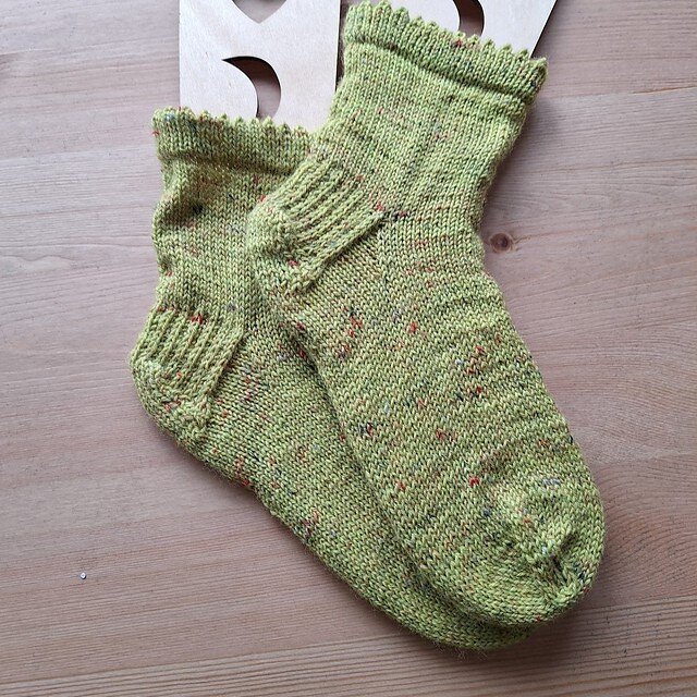 Bright green, handknit socks with speckles and a picot border on wooden sock blockers, laying on a wooden table