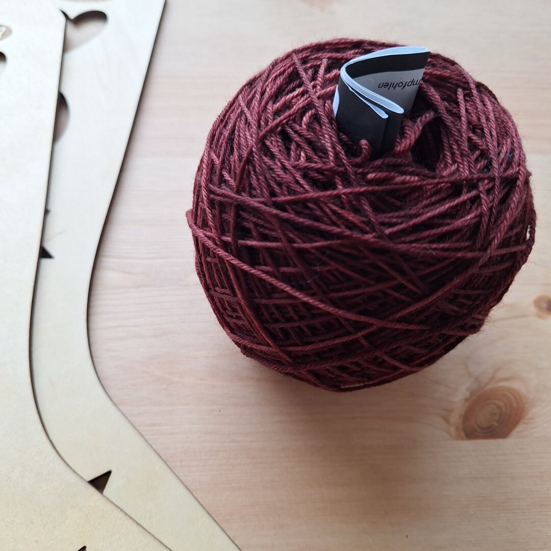 Burgundy red yarn caked up, with the label sticking out and sock blockers next to it