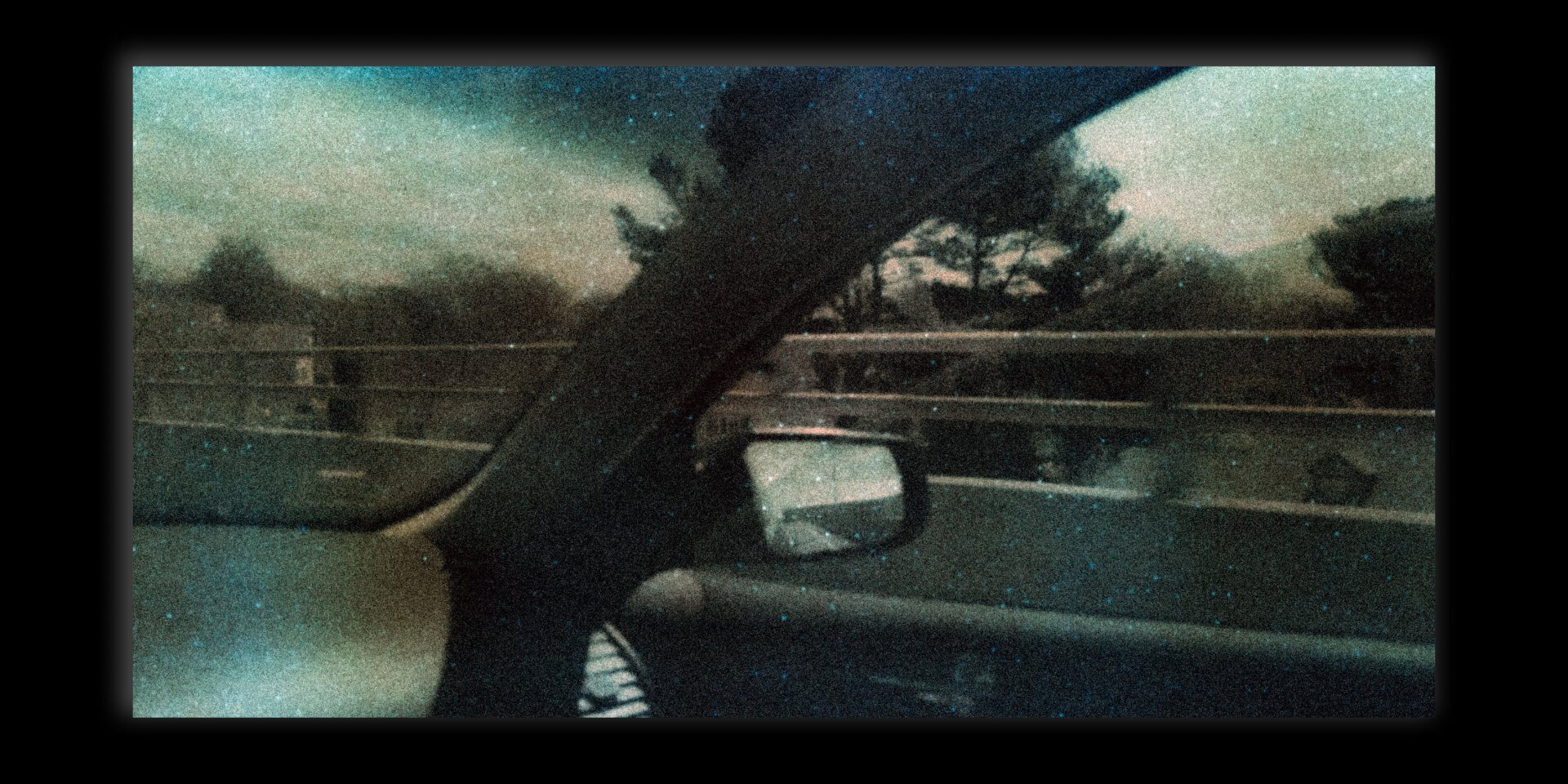 Grainy photograph showing the side view mirror of a car out the passenger window.