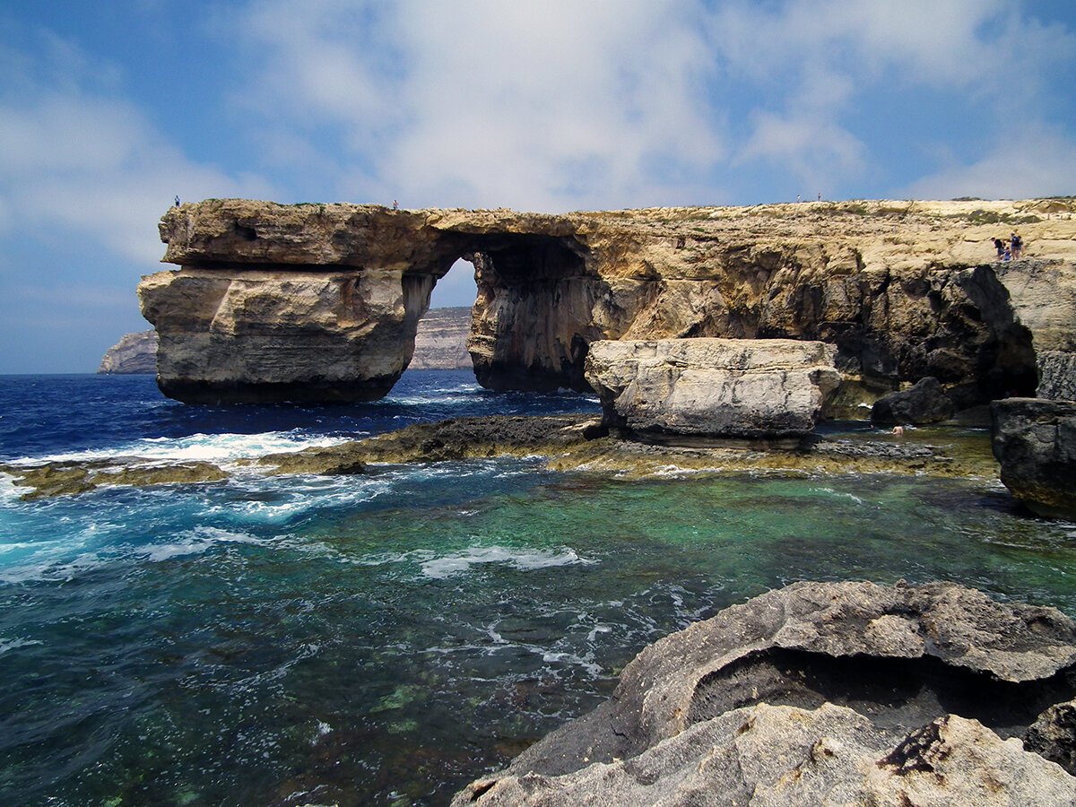 A rock-bridge thing in the blue sea, with blue sky.