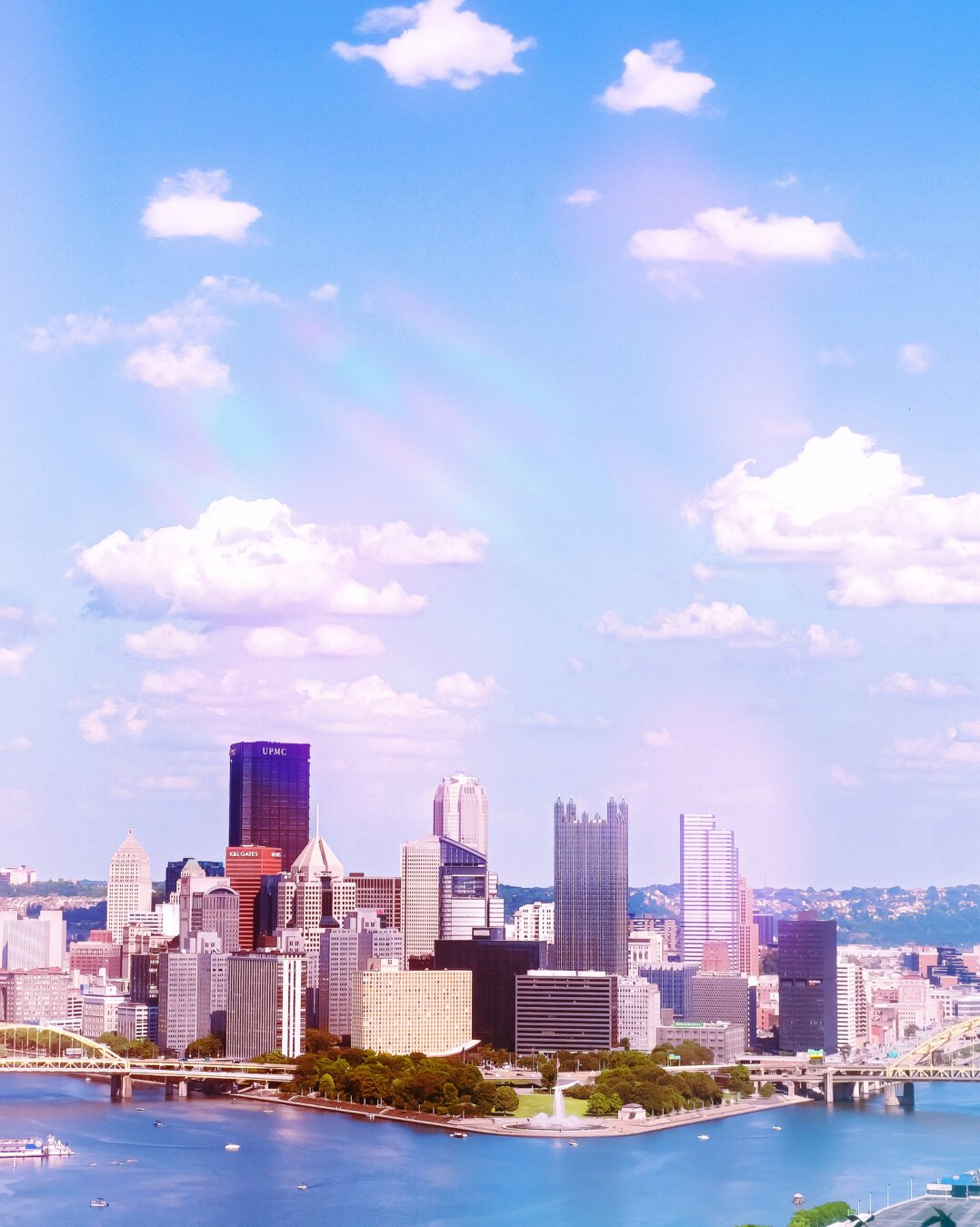 Skyline of Pittsburgh, Pennsylvania, with modern skyscrapers and the Allegheny River in the foreground under a partly cloudy sky.