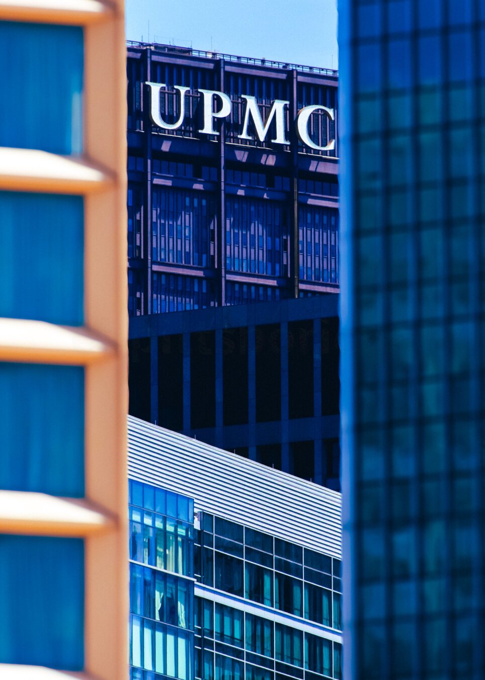 Modern skyscrapers of downtown Pittsburgh, PA, US, with reflective glass facades, one with 'UPMC' lettering at the top.