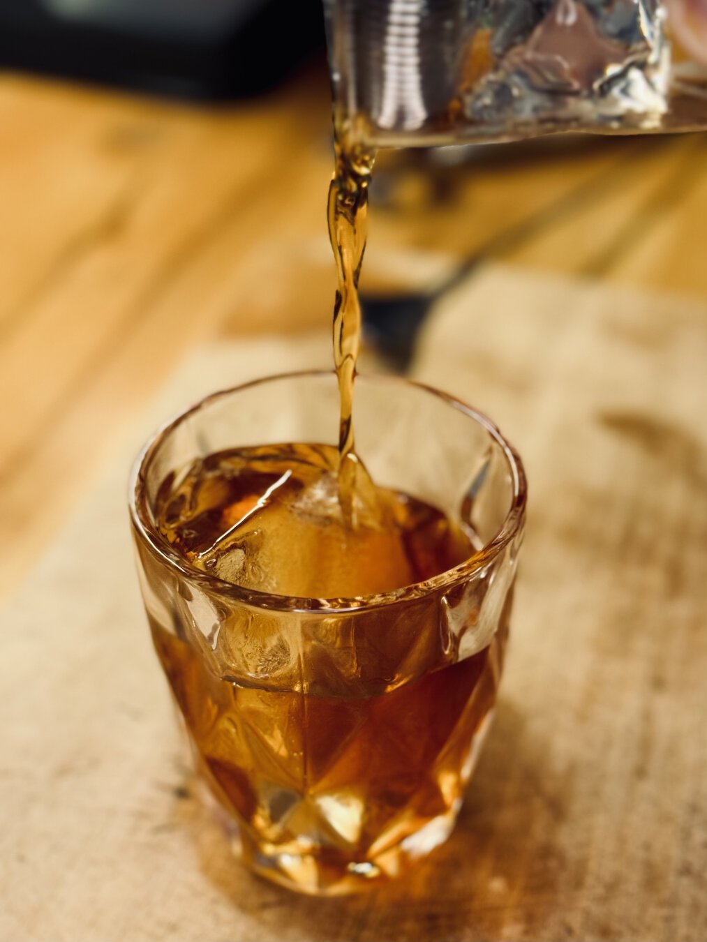 a golden brown cocktail being poured into a glass over a large rock of crystal clear ice
