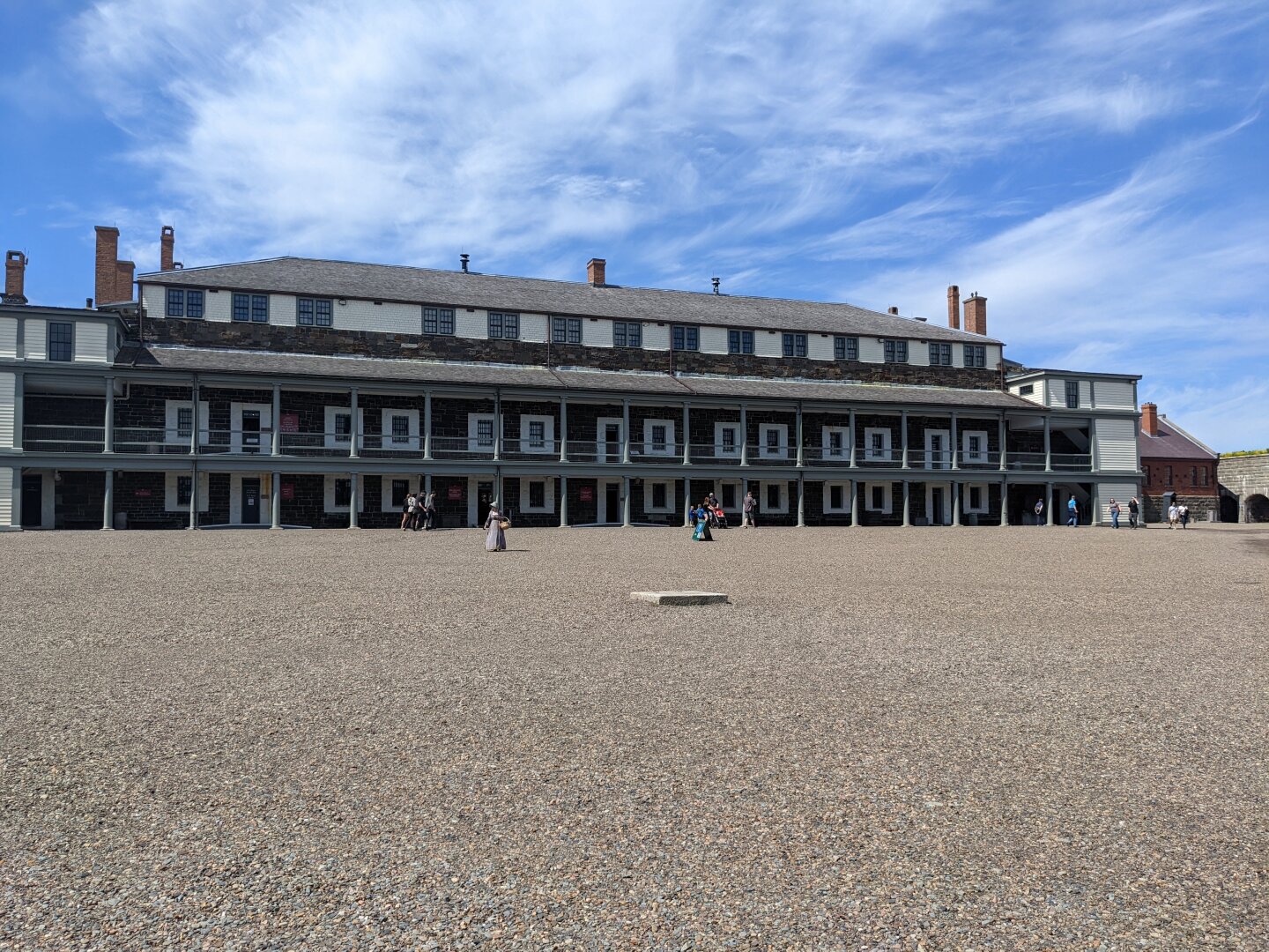An expansive gravel courtyard in front of an imposing colonial building under a partly cloudy sky