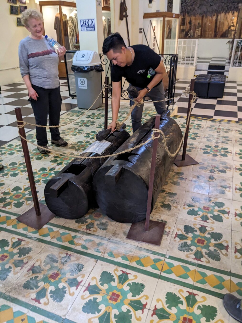 Two large black cylindrical instruments on a decorative tiled floor being played by a man in a black shirt.