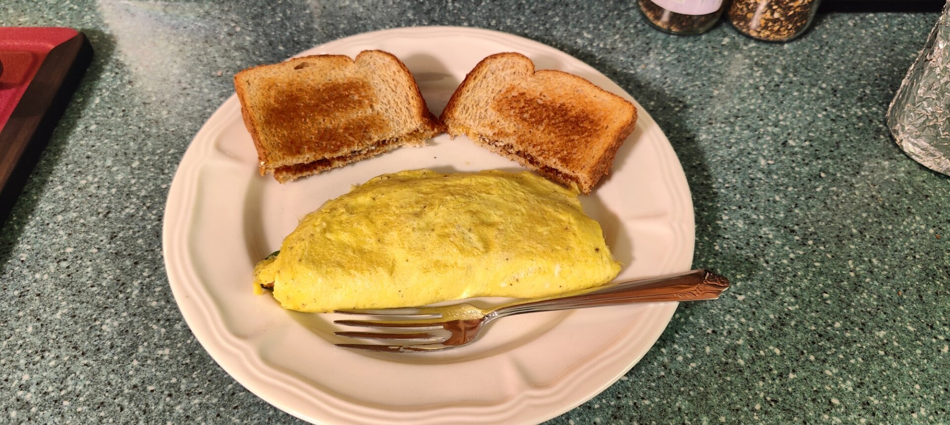 Ham and cheese omelette with spinach. 
Side of buttered toast. 
Displayed whole.