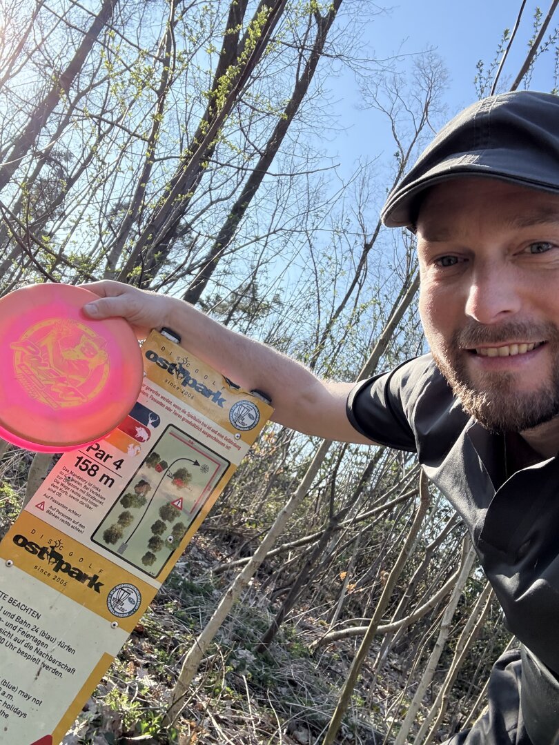 Wolf holding his Kat Mertsch #Polecat in front of the Rüsselsheim disc golf course for hole 24.