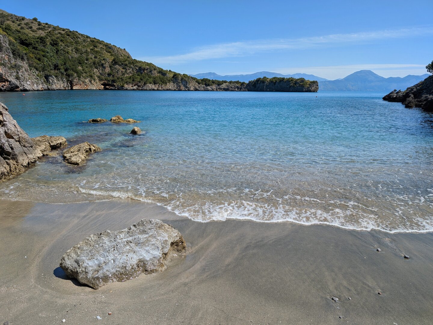 A wave from the crystal-clear sea crashes onto the sandy beach of Cala Infreschi.