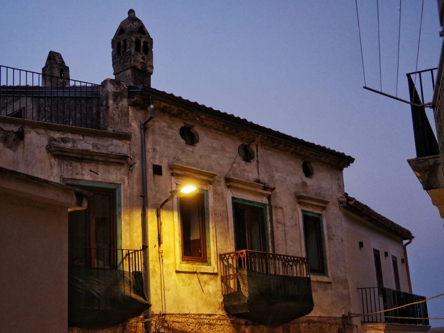 View of part of an upper house in Civita, illuminated by an external light placed near a window on the façade. A typical Civita chimney pot stands out on the roof