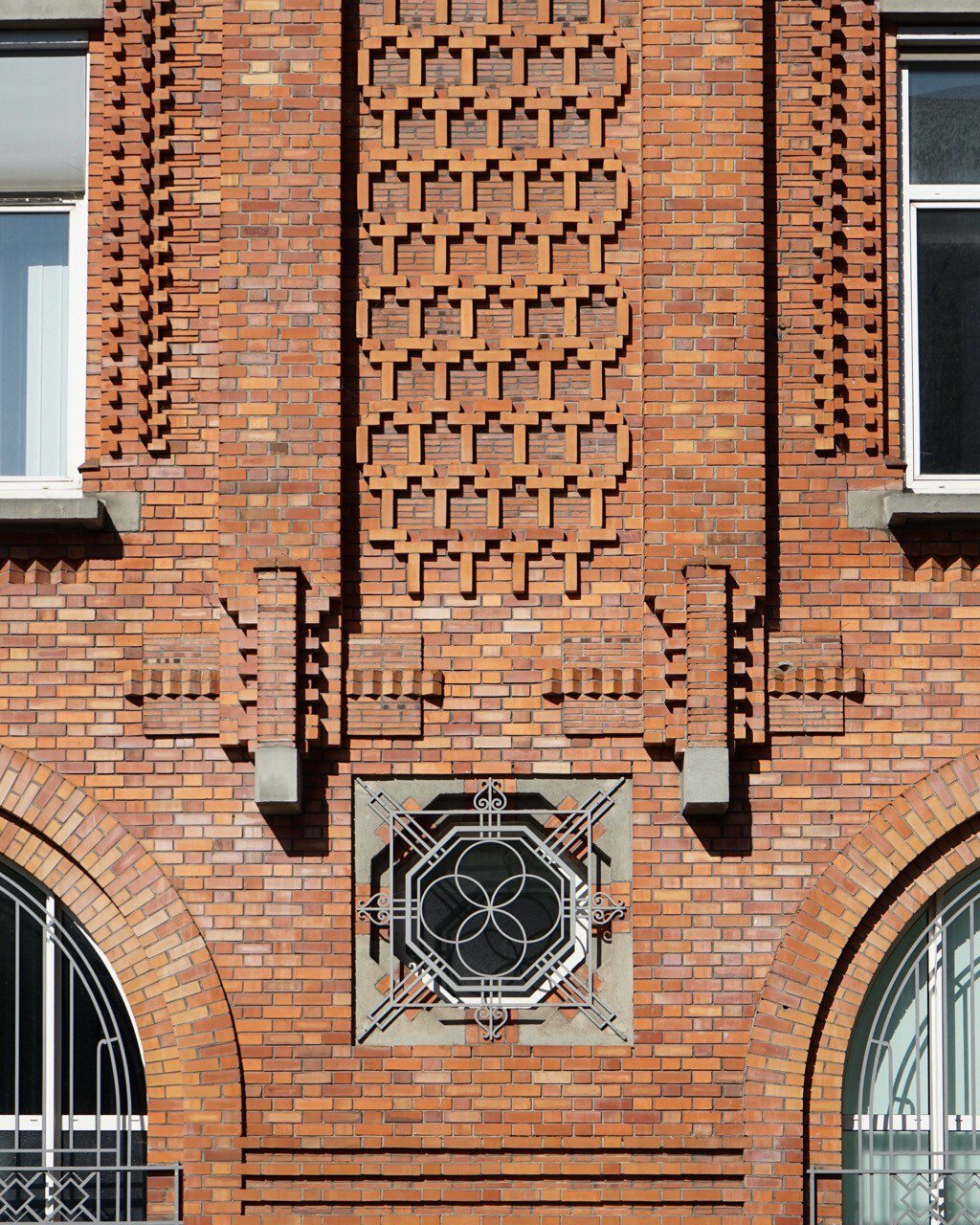 Façade en brique rouge mi Art déco mi expressionniste, avec des motifs en relief sophistiqués formant des alvéoles de briques, des verticales soulignées elles aussi par des motifs en relief, et des ferronneries fignolées formant des motifs géométriques pour habiller les ouvertures.