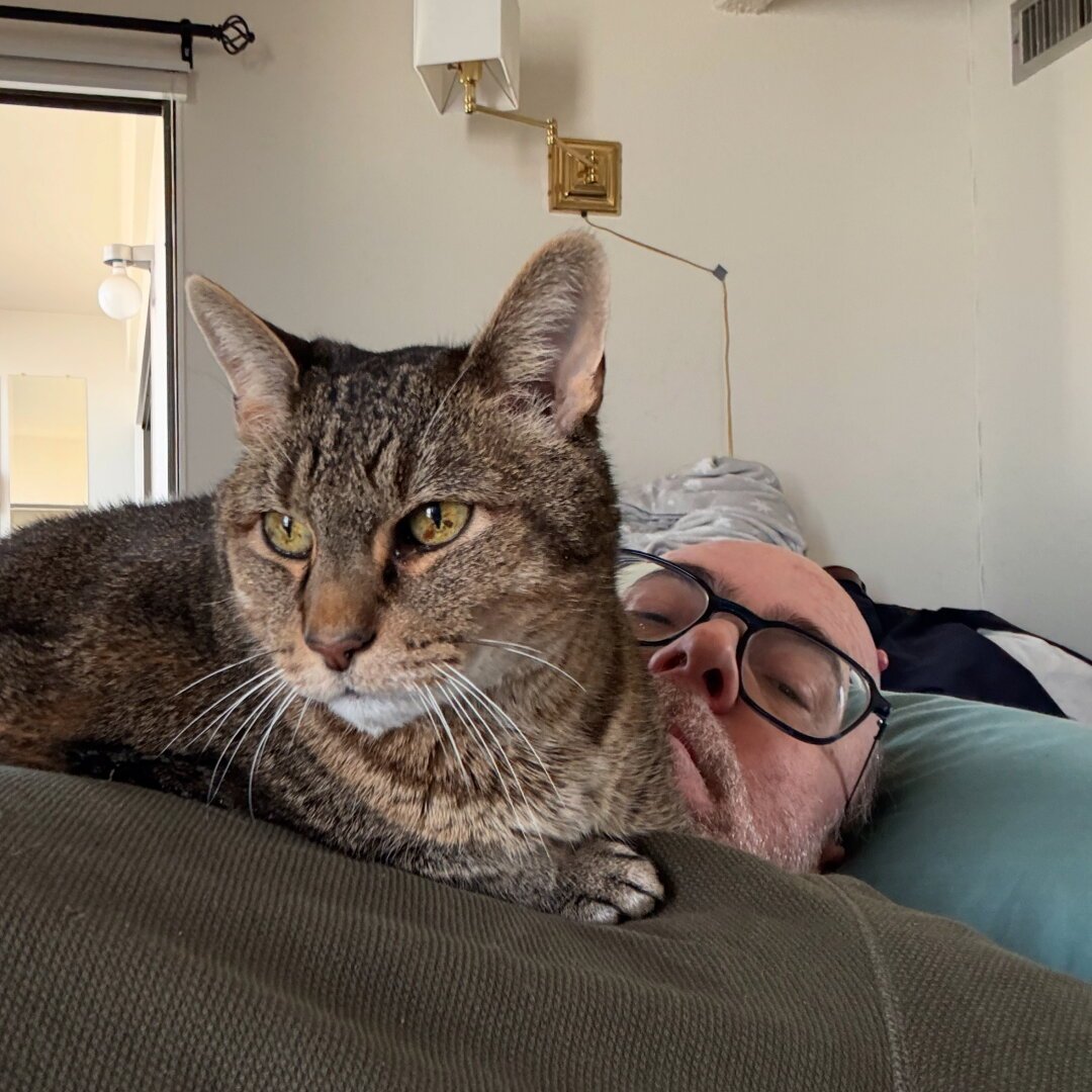 Me lying down with a cat on my chest, as he does.